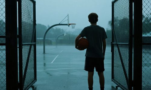 a young man unable to play basketball outside due to heavy rain and bad weather a young man unable to play basketball outside due to heavy rain and bad weather